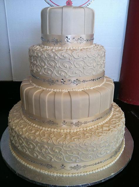 4 tier white wedding cake with rhinestone accents and swirled fondant design.